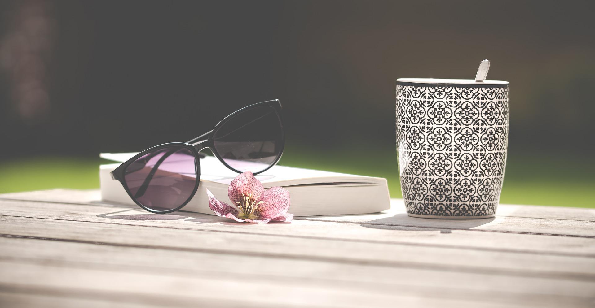 Une table de jardin sur laquelle sont posés un livre, une tasse de café et des lunettes de soleil
