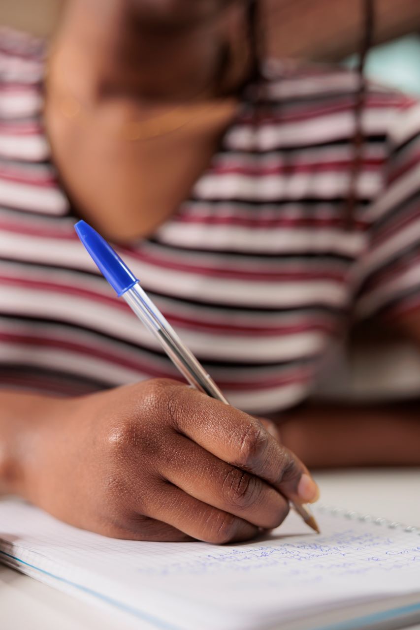 Un gros plan sur la main femme qui écrit sur un bloc de feuille à l'aide d'un stylo-bille